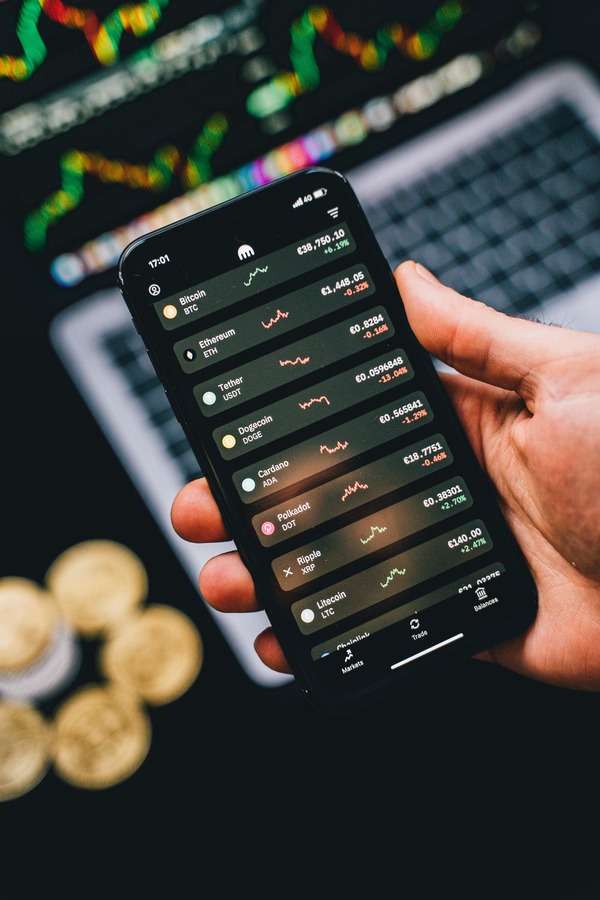Hand holding a phone with a crypto app above coins