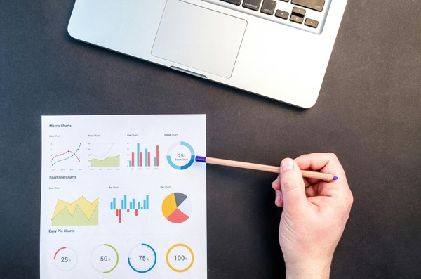 Hand pointing at printed charts next to a laptop