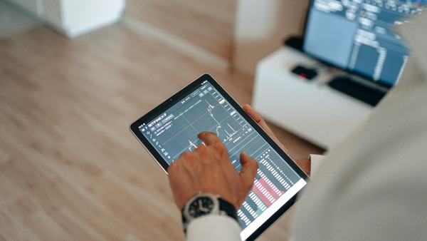 Hand using a tablet with a trading chart